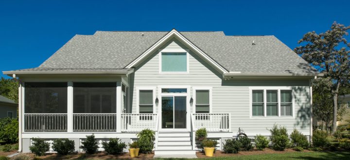 A modern home exterior featuring a gabled roof and a screened porch, surrounded by neat landscaping under a clear blue sky.