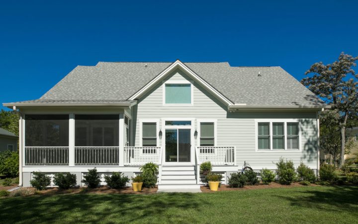 A modern home exterior featuring a gabled roof and a screened porch, surrounded by neat landscaping under a clear blue sky.