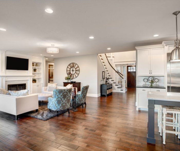 An expansive open concept living space with a white built-in media center, dark hardwood floors, and a connected kitchen area, elegantly designed for seamless living and entertaining.