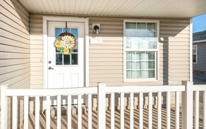Front porch of a charming home featuring a white door with a decorative wreath and surrounded by white railing.