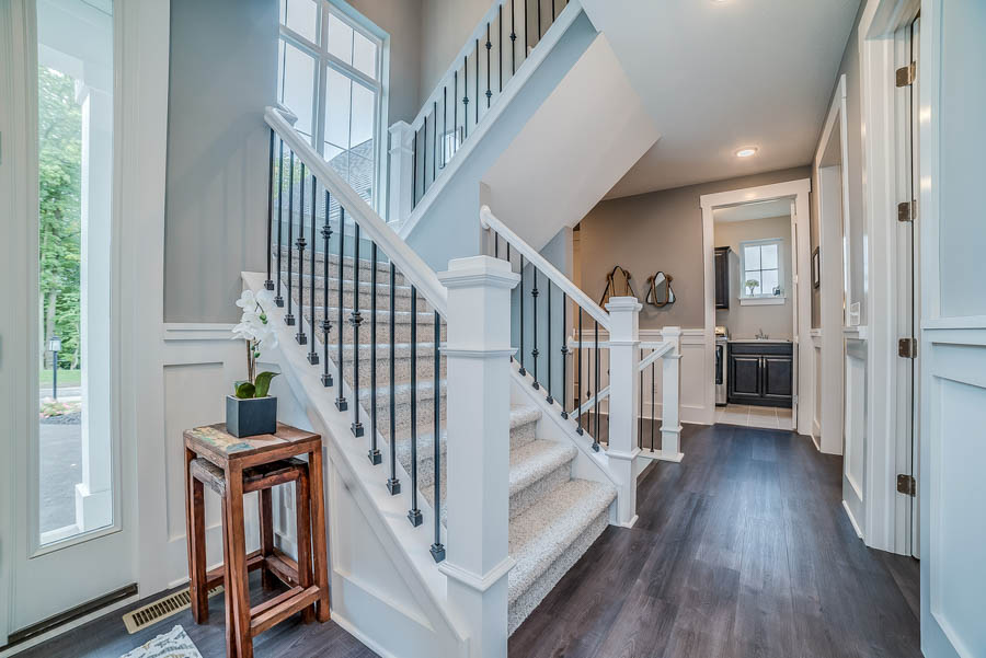 A bright and welcoming entryway featuring a white staircase with black metal balusters, highlighted by natural light and stylish decor.