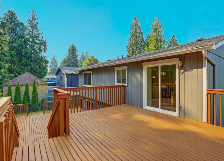 A broad wooden deck with railing, featuring sliding glass doors leading into the home, offering a scenic view of the surrounding greenery and residential area.