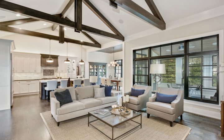 An elegant interior view of a luxury home with high ceilings supported by dark wooden beams, blending modern and traditional decor elements in a neutral color palette.