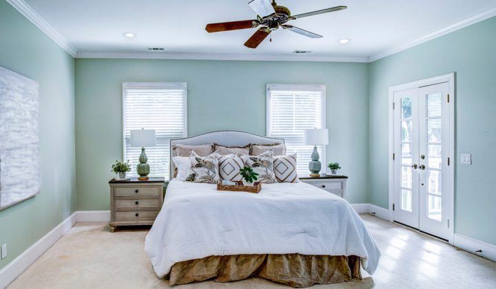 Serene master bedroom painted in soft green, featuring a bed with white linens and direct access to the outdoors through French doors.