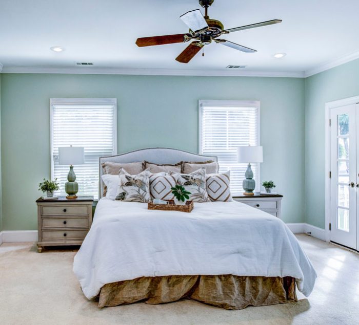Serene master bedroom painted in soft green, featuring a bed with white linens and direct access to the outdoors through French doors.