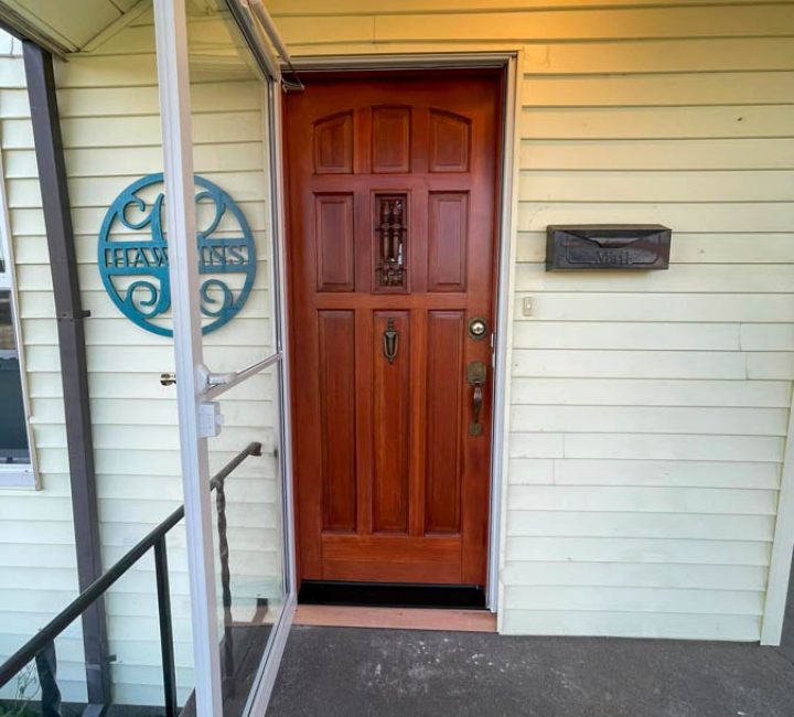 A traditional wooden door with ornate carvings and a decorative glass pane, set in a home with light siding and a welcoming porch light.