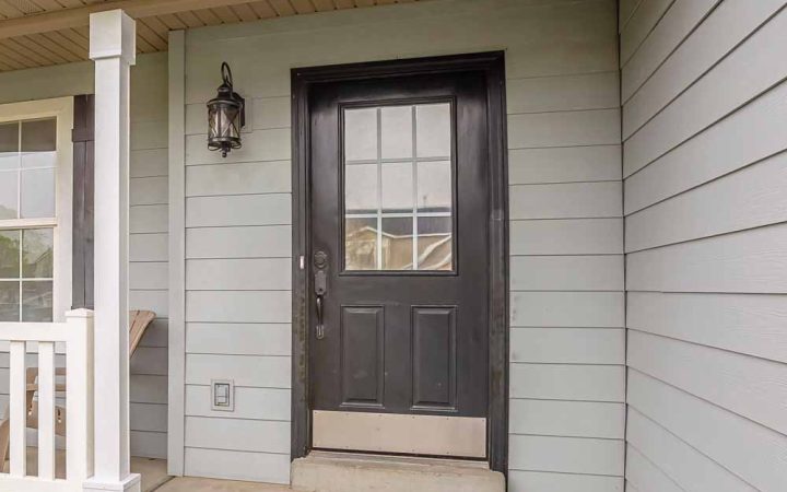 Front view of a house featuring a black door with glass panels under a covered porch, flanked by white columns and a wall lantern.